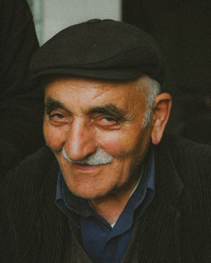 An elderly man in a flat cap, smiling warmly