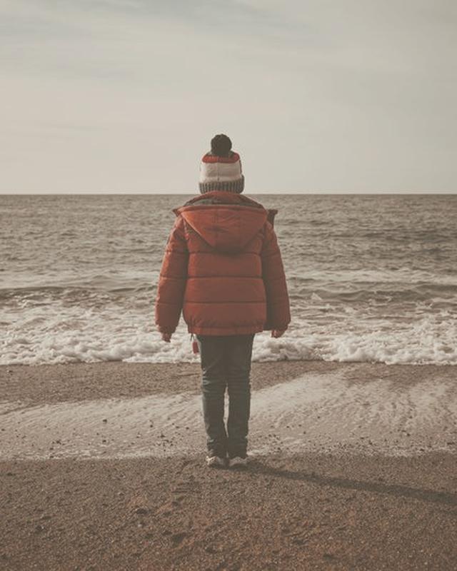 A faded colour photograph of a child alone on a beach in a red coat