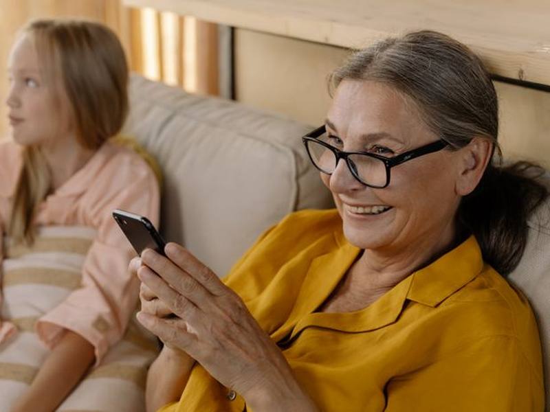 An older woman holding a phone with her granddaughter beside her